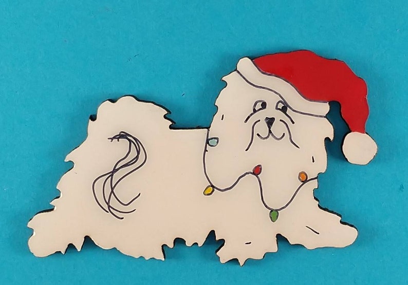 May include: A white dog-shaped Christmas ornament wearing a red Santa hat and a string of colorful lights. The dog has black outlines and a whimsical design, perfect for holiday decor.