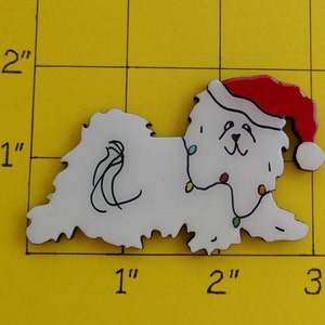 May include: A white dog-shaped Christmas ornament, approximately 2 inches long, wearing a red Santa hat and a string of colorful lights. The ornament has black details and is on a yellow grid background.