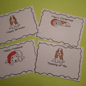 May include: Four white greeting cards with black scalloped borders and dog illustrations. The cards have text that reads "Happy Birthday", "Merry Christmas", "Happy Holidays", and "Thinking of You". The background is a light green.