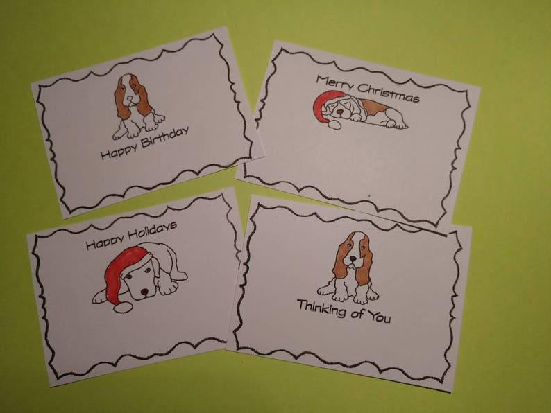 May include: Four white greeting cards with black scalloped borders and dog illustrations. The cards have text that reads "Happy Birthday", "Merry Christmas", "Happy Holidays", and "Thinking of You". The background is a light green.