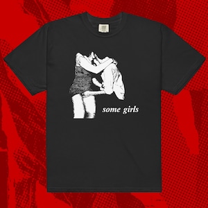 May include: Black t-shirt with a white graphic of two people embracing. The text "some girls" is printed below the graphic.