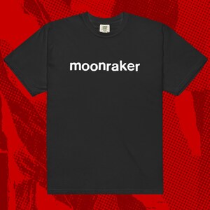 Pode incluir: Camiseta preta com a palavra "moonraker" impressa em branco no centro. A camiseta tem mangas curtas e gola redonda. O fundo é um padrão de meio-tom vermelho e preto.