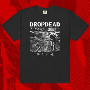 Puede incluir: Camiseta negra con texto blanco "DROPDEAD" sobre una imagen en escala de grises de una persona en vías de tren. Texto japonés debajo de la imagen.