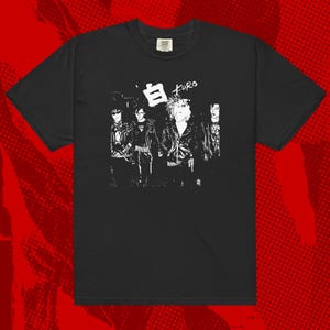 May include: Black t-shirt featuring a white graphic of a band with the text "白 Kuro". The illustration depicts four figures in a punk rock style. The shirt has a crew neck and short sleeves.