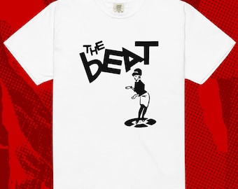 Puede incluir: Camiseta blanca con la inscripción negra "THE BEAT" y una ilustración estilizada de una mujer bailando sobre un disco. La camiseta tiene mangas cortas y cuello redondo.