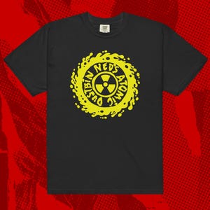 Może przedstawiać: Czarny T-shirt z żółtym nadrukiem w kształcie koła z tekstem "Ned's Atomic Dustbin" i symbolem radioaktywnym w środku.