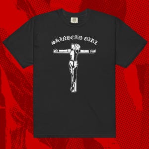 May include: Black t-shirt with a white graphic of a person on a cross. The text "SKINHEAD GIRL" is above the graphic.
