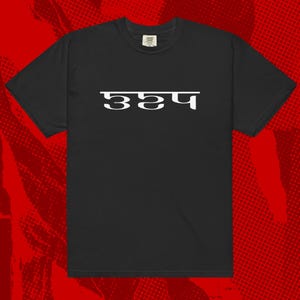 May include: Black t-shirt featuring white text in a unique font. The text is in a non-English script. The shirt has a crew neck and short sleeves. The background is a red and black halftone pattern.