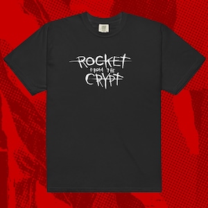 May include: Black t-shirt with a white graphic that says "ROCKET from the CRYPT" with a line through the word "ROCKET".