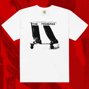 May include: White t-shirt with a black and white graphic of a person's legs and feet on a skateboard. The text "THE FRUMPIES" is above the graphic in black letters. The shirt has a crew neck and short sleeves.