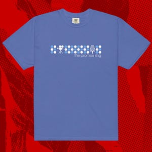 Könnte beinhalten: Ein blaues Kurzarm-T-Shirt mit einem grafischen Design. Das Design zeigt eine Reihe weißer und blauer Punkte, ein Kamera-Symbol und ein Mikrofon-Symbol. Der Text "the promise ring" steht darunter.