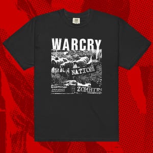 Op de afbeelding: Zwart t-shirt met een wit grafisch ontwerp. Het ontwerp bevat het woord "WARCRY" boven een illustratie van schapen, het woord "NATION" en het woord "ZOMBIES". Het shirt heeft ook de tekst "Avoid the walking herd, shun the polluted flock."