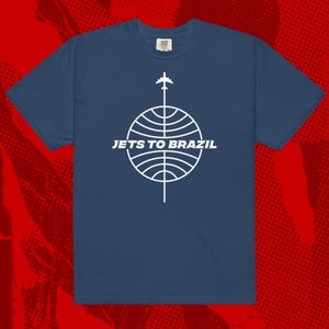 May include: A navy blue t-shirt with a white graphic of a globe with a plane flying over it. The text "Jets to Brazil" is printed below the globe.