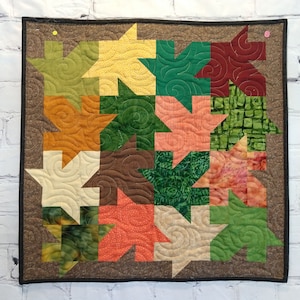 May include: A quilt with a brown background and a patchwork design of various colored leaves. The leaves are in shades of green, orange, red, and yellow. The quilt is quilted with a swirl pattern.