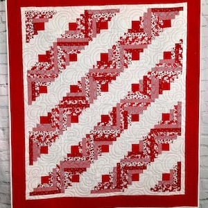 May include: A red and white quilt with a log cabin pattern. The quilt is quilted with a swirling design.