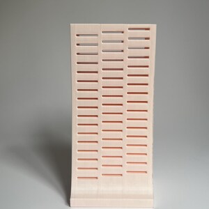 May include: A pale pink plastic organizer with a grid pattern. The organizer has a curved front and a flat back.
