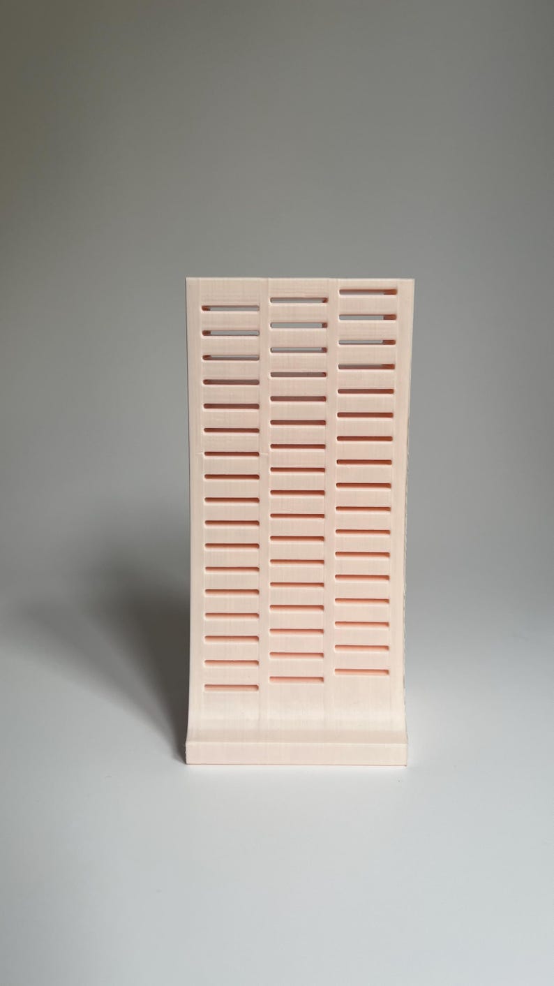 May include: A pale pink plastic organizer with a grid pattern. The organizer has a curved front and a flat back.