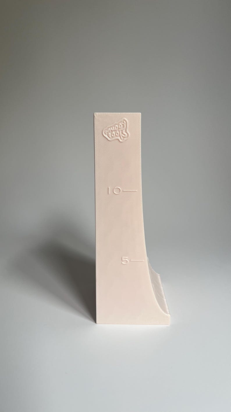 May include: A white plastic measuring tool with a curved edge and markings for 5 and 10. The tool has the words "Gooey Tools" embossed on the top.
