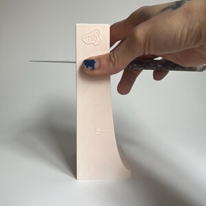 May include: A pink plastic tool with the words "Sugar Tools" embossed on it. The tool has a curved edge and markings for 5 and 10 inches.
