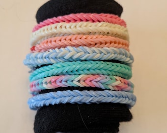 May include: A stack of colourful rubber band bracelets in pink, white, blue and turquoise. The bracelets are woven in a herringbone pattern.