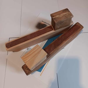 Może przedstawiać: Dwa drewniane elementy drewnianej maszynki do makaronu. Elementy są wykonane z jasnego drewna brązowego i mają ciemnobrązowe zabarwienie. Elementy są połączone metalowym kołkiem. Elementy są oznaczone "Wooden Pasta Maker".