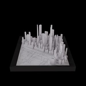 Op de afbeelding: Een wit 3D-model van een stadsbeeld, inclusief wolkenkrabbers en gebouwen, geplaatst op een getextureerde basis. Het model is ingelijst in een zwart frame.
