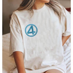 Peut inclure: T-shirt crème avec un numéro 4 bleu brodé dans un cercle. Le t-shirt a des manches courtes et une coupe décontractée, adapté aux tenues décontractées.