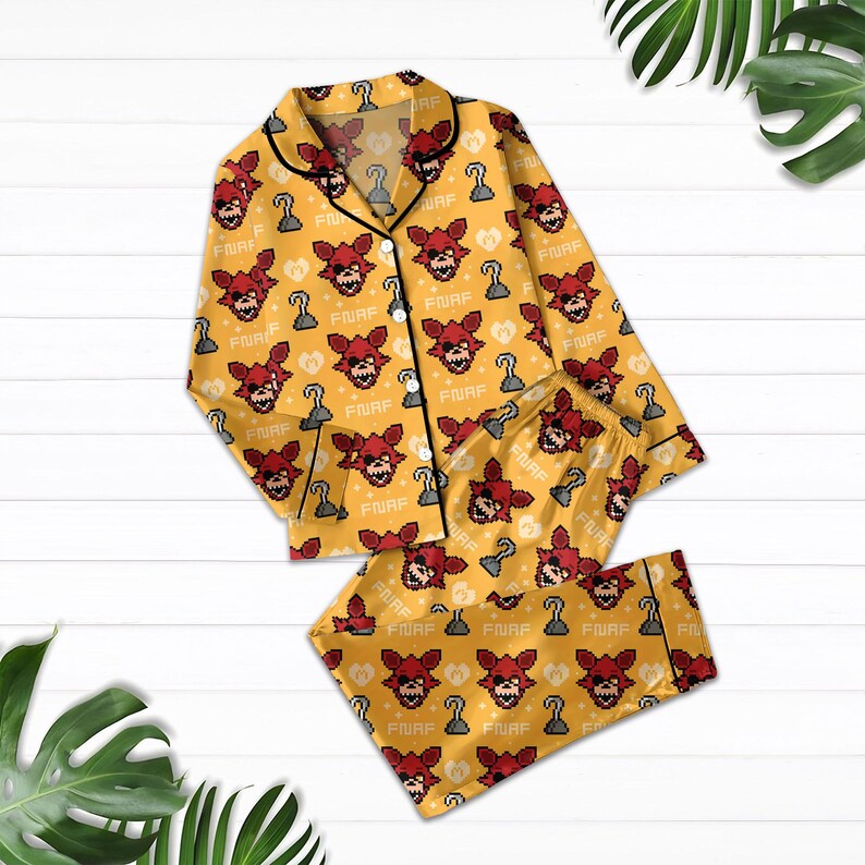 May include: Yellow pajama set with a repeating pattern of a red fox face, a hook, and the word "FURF". The long-sleeved top has black trim and buttons. The pajama bottoms are shorts.