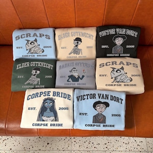 May include: Nine sweatshirts with various character designs from the movie Corpse Bride. Each sweatshirt features a different character, the text "CORPSE BRIDE", and the year "2005". The sweatshirts are in various colors, including blue, green, and black.