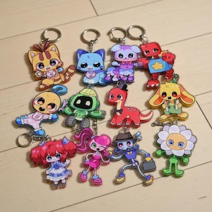 Puede incluir: Una colección de llaveros de personajes de dibujos animados coloridos. Los llaveros presentan varios diseños de animales y personajes, incluyendo un gato, un perro, un robot, un dinosaurio y una flor. Cada llavero tiene un anillo de metal plateado.