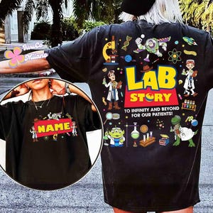 May include: Black t-shirt with a colorful "Lab Story" design featuring cartoon characters, lab equipment, and the text "To infinity and beyond for our patients!" A smaller image on the front has the word "NAME" on a red background.