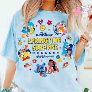 May include: Light blue t-shirt featuring the text "runDisney SPRINGTIME SURPRISE WEEKEND Walt Disney World". The shirt has colorful graphics of Disney characters and icons, including Winnie the Pooh, Stitch, and Aladdin. A fun and vibrant design.