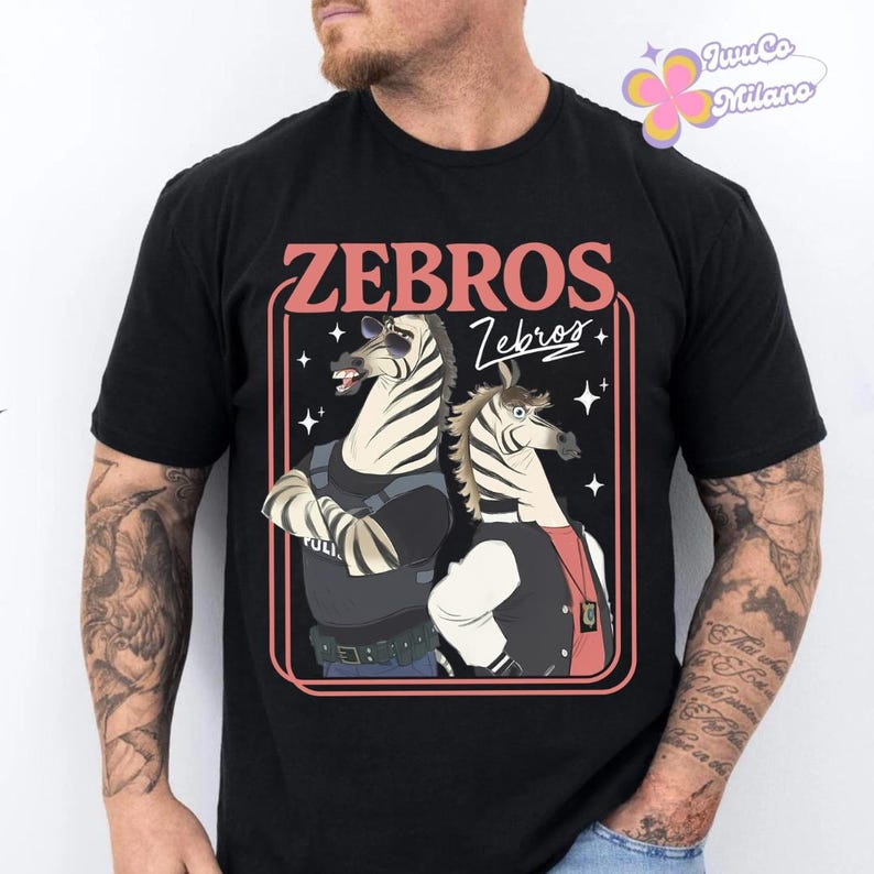 May include: Black t-shirt featuring a cartoon illustration of two zebras. The design includes the word "ZEBROS" in a retro font, with one zebra wearing sunglasses and a police uniform, and the other in a letterman jacket.