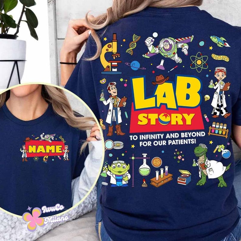 May include: Navy blue t-shirt with a colorful graphic design. The design features the words "LAB STORY" in yellow and red, along with cartoon characters and science-themed illustrations. The text "TO INFINITY AND BEYOND FOR OUR PATIENTS!" is also included.