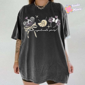 May include: Dark gray t-shirt featuring a whimsical graphic with the text "Poor unfortunate souls!" The design includes cartoon elements like a bow, seashell, and a headband with a bow. The shirt has short sleeves and a relaxed fit.