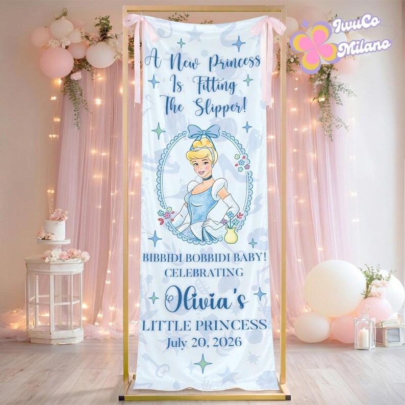 May include: A white banner with a Cinderella theme, featuring the text "A New Princess Is Fitting The Slipper!" and "Olivia's Little Princess July 20, 2026." The banner has a gold frame and is decorated with pink bows and balloons.