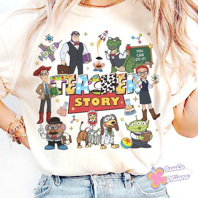 K&ouml;nnte beinhalten: Cremefarbenes T-Shirt mit einer farbenfrohen Grafik von Toy Story-Charakteren in einem Klassenzimmer. Die Worte "TEACHER STORY" sind prominent dargestellt. Das Design beinhaltet eine Rakete, einen Apfel und den Satz "YOU CAN DO IT!"