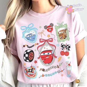 Puede incluir: Camiseta rosa con un estampado gr&aacute;fico de coches de dibujos animados, corazones, cerezas y un batido. El texto "Mater" y "Sally" est&aacute; impreso en la camiseta.