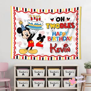 May include: A rectangular fabric banner featuring Mickey Mouse wearing a party hat and holding a birthday cake. The text reads OH TWODLES HAPPY BIRTHDAY KEVIN with a large number 2. The border has red, black, and yellow stripes with wavy lines.