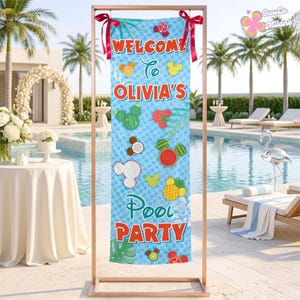 May include: A vertical rectangular banner hanging from a copper-colored metal stand with red ribbons. The light blue banner features the text "WELCOME TO OLIVIA'S POOL PARTY" in red and green, decorated with various fruit-shaped icons resembling mouse ears.