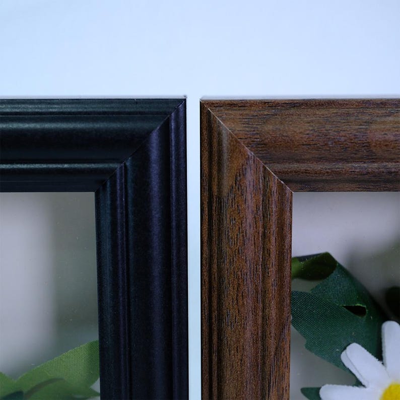 May include: Close-up of two picture frames. One frame is black, the other is brown with a wood grain pattern. Both frames have a beveled edge. The frames are empty, with a white background visible.