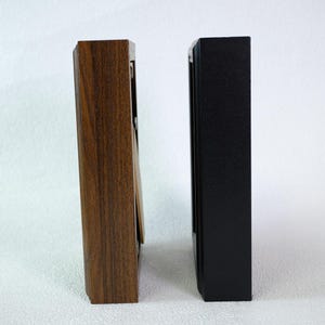 May include: Two rectangular picture frames. One frame is made of dark brown wood with a visible wood grain. The other frame is black. Both frames are standing upright and are empty.