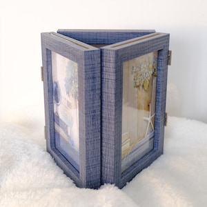 May include: A blue wooden picture frame with three hinged panels. Each panel displays a different image, with a coastal theme. The frame is made of wood and has a distressed finish. The panels are connected by brass hinges.