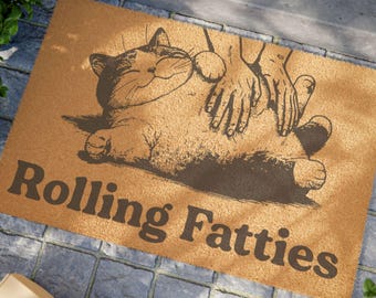 May include: A brown rectangular doormat featuring a cat illustration and the words "Rolling Fatties". The cat is depicted lying down with hands petting it. The mat has a textured surface, and the text is in dark brown.