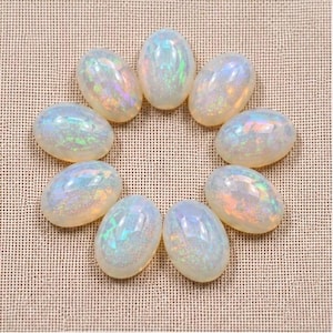 May include: A collection of nine oval-shaped, cabochon-cut opals arranged in a circular pattern. Each gemstone features a milky white base with iridescent flashes of green, blue, and pink light reflecting across the smooth, polished surfaces.