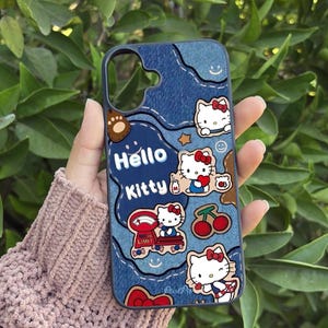 May include: A blue denim-style phone case featuring Hello Kitty designs. The case has a patchwork design with various Hello Kitty illustrations, cherries, and stars. The words "Hello Kitty" are prominently displayed on the case.