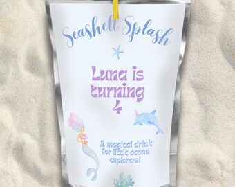 May include: A silver pouch with a white label that says "Seashell Splash" and "Luna is turning 4". The label has a mermaid, a dolphin, and a starfish. The text "A magical drink for little ocean explorers!" is also on the label.