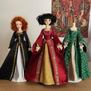 May include: Three dolls wearing different renaissance era gowns. The doll on the left is wearing a black gown with gold trim, the doll in the middle is wearing a red gown with gold trim and a gold patterned skirt, and the doll on the right is wearing a green gown with a floral pattern.