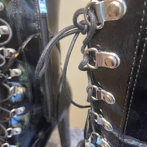 May include: Black patent leather boots with silver buckles and a lace-up front. The boots have a chunky heel and a zipper on the side.