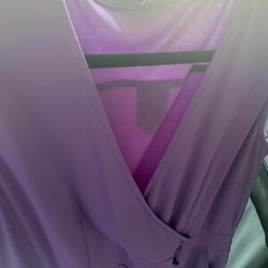 May include: A purple sleeveless jumpsuit with a deep V-neckline and a wrap-style bodice.